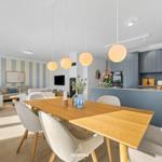 Dining area with wooden table and chairs, kitchen with blue cabinets and living room with striped wall.