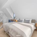 Bedroom with sloped ceiling, bed, nightstand, and desk.