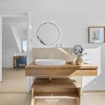 Bathroom with wooden vanity, round mirror, and flowers.