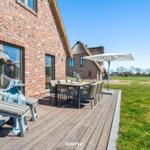 Deck with seating, table, and umbrella next to a brick house.