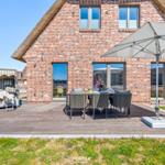Terrasse mit Tisch, Stühlen und Sonnenschirm vor einem Backsteinhaus mit Strohdach.