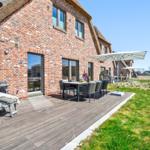 Terrasse mit Tisch, Stühlen und Sonnenschirm neben einem Backsteinhaus mit Strohdach.