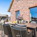 Terrasse mit Esstisch, Stühlen und Blick auf Backsteinhaus.