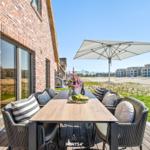 Terrasse mit Tisch, Stühlen und Sonnenschutz neben Backsteinhaus.