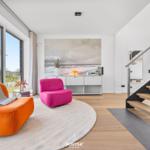 Wohnzimmer mit orangefarbenem Sofa, pinkem Sessel und Blick auf den Garten.
