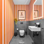 Badezimmer mit orangefarbenen Streifen an den Wänden und grauen Fliesen.