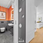 Badezimmer mit orangefarbenen Streifen und moderner Einrichtung. Blick in die Küche.