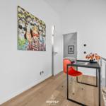 Schlafzimmer mit Schreibtisch, roter Stuhl und Wandbild.