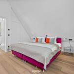 Schlafzimmer mit pinkem Bett und Holzboden unter schräger Decke.