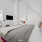 Schlafzimmer mit Dachschrägen, Bett, TV und angrenzender Toilette.