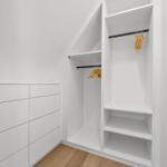 Weißer Schrank mit Kleiderstangen und Ablageflächen, Holzboden und schräge Decke.