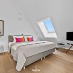 Schlafzimmer mit Dachfenster, Bett, TV und Nachttisch.