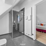 Badezimmer mit Dusche und angrenzender Schlafzimmer mit Bett.