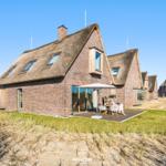 Haus mit Strohdach, Terrasse und Garten. Modernes Design mit Holz und Glas.