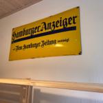 Gelbes Schild mit Schriftzug an Wand über Holzbank