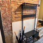Schwarzer Garderobenstuhl vor Backsteinwand mit Regal und Schublade.