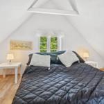 Bedroom with sloped ceiling, bed, two nightstands, and window with view of greenery.