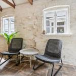 Two chairs and a table are positioned by a window in a room with stone wall and wooden beams.