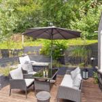Terrace with seating group, umbrella, and plants. Wooden terrace beside house wall.