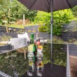 Terrace with table, seating, and umbrella. Background: green plants and wooden wall.