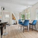 Dining area with blue chairs and wooden floor. Kitchen with bar and windows.