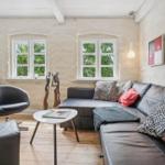 Living room with sofa, seating, and windows overlooking greenery.
