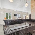 Kitchen with dark mosaic tiles and white worktop. Windows with view of greenery.