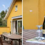 Terrace with table, chairs, and umbrella in front of yellow house. Table with wine bottle and book.