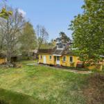 Yellow house with garden and trees under blue sky.