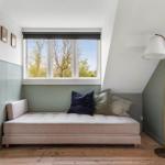 A bedroom with a sloped ceiling, window, and sofa with cushions.