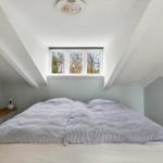 Bedroom with sloped ceiling, window, and bed with striped bedding.