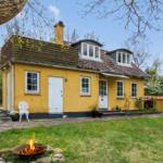 Yellow house with dormer windows and garden. A fire pit burns in the foreground.