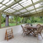 Patio with table and chairs under roof, view of green surroundings.