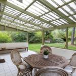 Terrace with table, chairs, and glass roof. View of green garden.