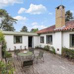 A house with white walls and red roof has a paved courtyard with table and chairs.