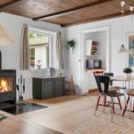 A room with fireplace, dining table, and kitchen area. Wooden ceiling and floor.