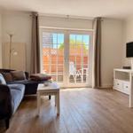 Wohnzimmer mit Sofa, Tisch und TV. Durchgehende Glastür zum Balkon mit Garten.