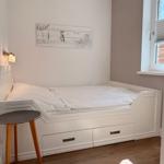 Schlafzimmer mit weißem Bett, kleiner Tisch und Wandbild.