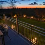 Terrasse mit Tisch und Stühlen, beleuchteter Garten und Landschaft bei Sonnenuntergang.