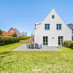 White villa with garden and terrace. Table and chairs on paved area.