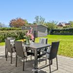 Patio with table and chairs, surrounded by lawn and hedge.
