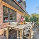 Terrace with wooden table, chairs, and flowers in front of brick house