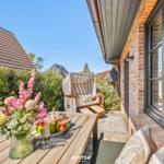 Terrace with wooden table, flowers, and lounge chair in front of brick house