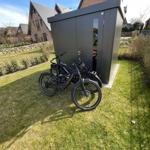 Two black bicycles stand in front of a gray shed in the garden.
