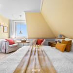Bedroom with sloped ceiling, bed, armchairs, and window.