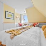 Bedroom with sloped ceiling, bed with pillows and wall art.