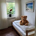 Ein Bett mit einem Plüschbären darauf, ein Fenster mit Blick auf Grün und eine Wanddekoration.