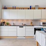 Küche mit weißen Schränken, Arbeitsfläche und Küchengeräten. Tisch mit Tischdecke und Stühlen.