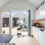 Küche mit Blick auf Terrasse und Gartenhaus. Weiße Schränke, Arbeitsplatte und Spüle.