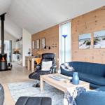 Wohnzimmer mit Kamin, Sofa und Küchenbereich. Holzwand und Strandbilder.